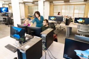 People working together at a computer in a well-lit, pleasant space with multiple computing workstations. 