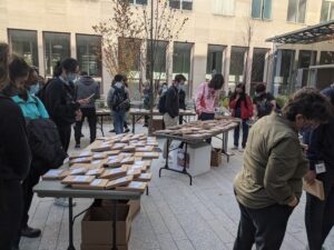 A crowd of people gather in a courtyard looking at books wrapped in brown paper
