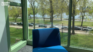 Blue chair in front of a window bay overlooking a street with cars and a river