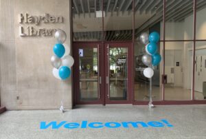 Hayden Library entrance flanked by bunches of silver and blue balloons; there is a blue "Welcome" sign on the floor in front of the door