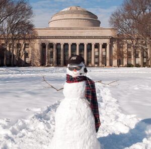 A snowman on Killian Court wears a scarf and an MIT cap