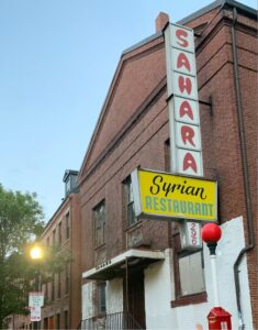 A building with a brick facade and a sign reading Sahara Syrian Restaurant