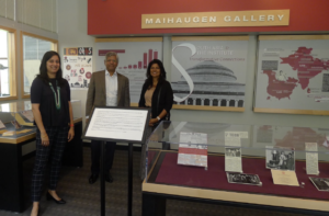 Three people stand next to a display case in the exhibit "South Asia and the Institute."