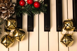 Holly and gold bells on a piano keyboard.