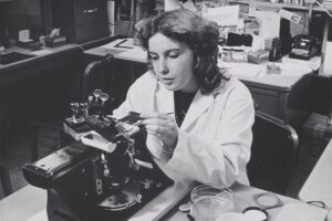 Black and white photo of a woman in a lab coat in a lab