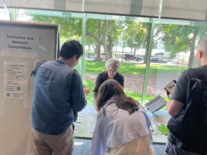 People stand in front of a table that is staffed by a librarian; there is a sign next to the table that reads "Instruction and Research Consultations."