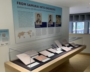 Display case with historic documents and a poster with text and photos of early Japanese students